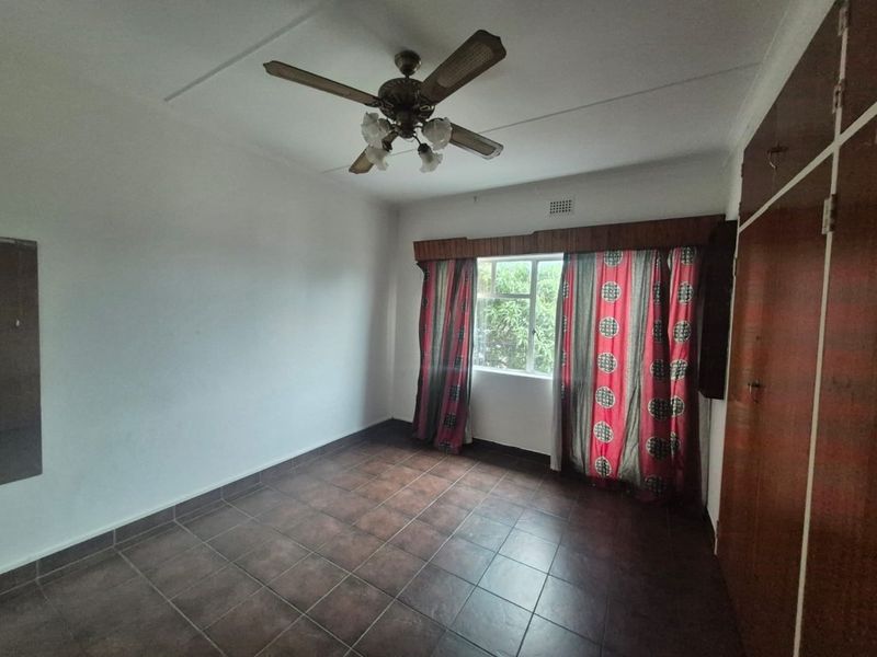 A spacious bedroom featuring tiled flooring, a ceiling fan, and built-in wooden cupboards, offering a clean and functional space ready for personalization.
