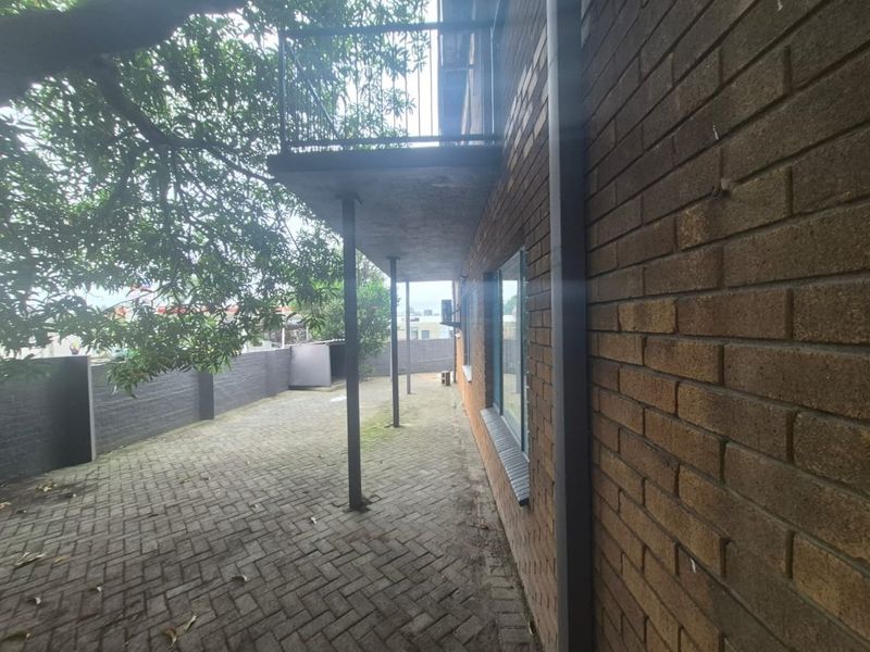 Rear exterior view of the flat featuring a paved courtyard area, brick facade, and an overhead balcony with metal railings.