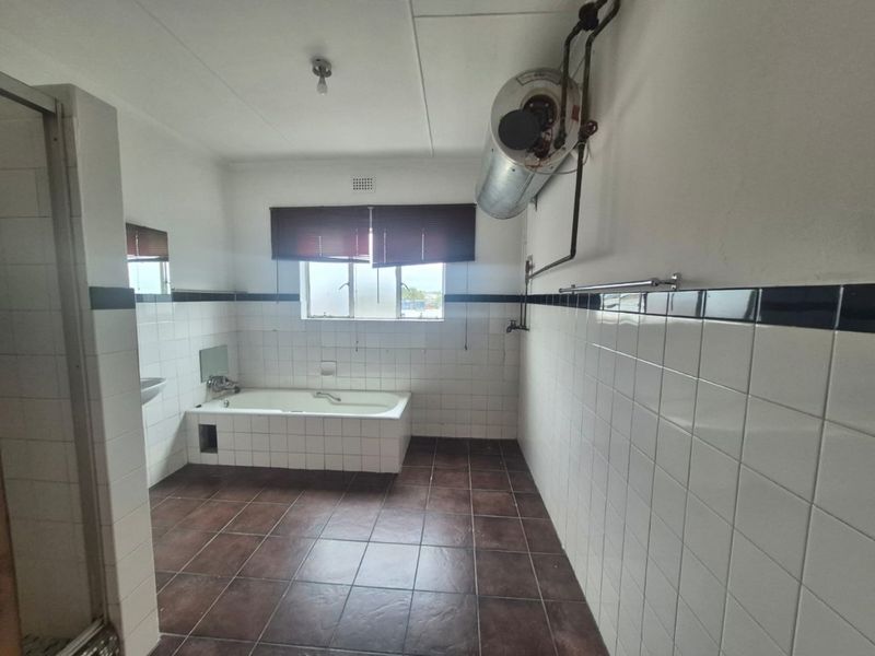 Spacious bathroom featuring a built-in bathtub, shower enclosure, and wall-mounted geyser, finished with classic tiled walls and flooring.