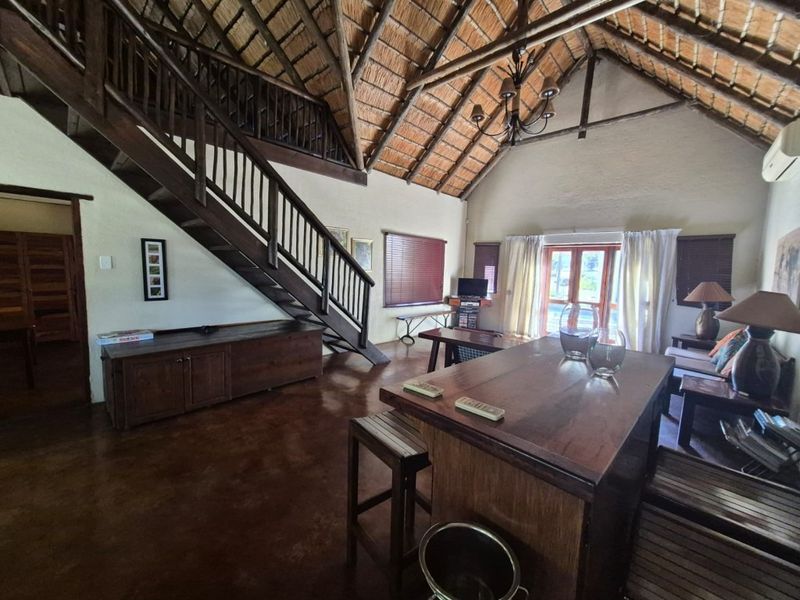 Spacious open-plan living area featuring a high vaulted thatched ceiling with exposed timber trusses, a wooden staircase, and polished concrete flooring.