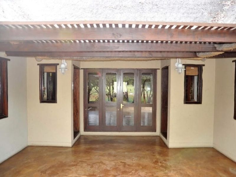 A covered outdoor patio area featuring a timber pergola, concrete flooring, and glass-paneled french doors leading to the garden.