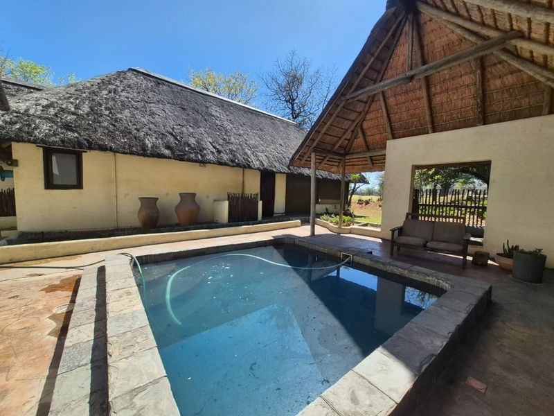 Outdoor pool area featuring a stone-tiled surround and a covered patio with a traditional thatched roof structure.