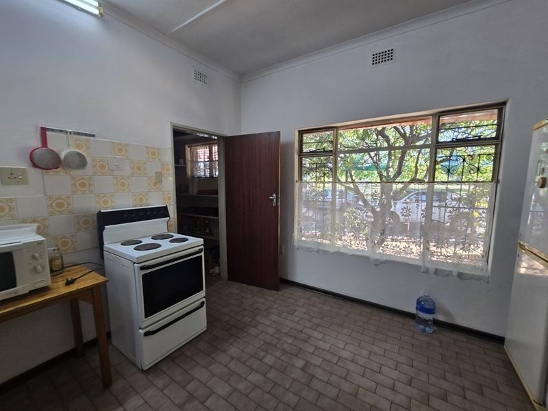 A functional kitchen featuring tiled flooring, a freestanding stove, and a large window with security bars, offering potential for modernization.