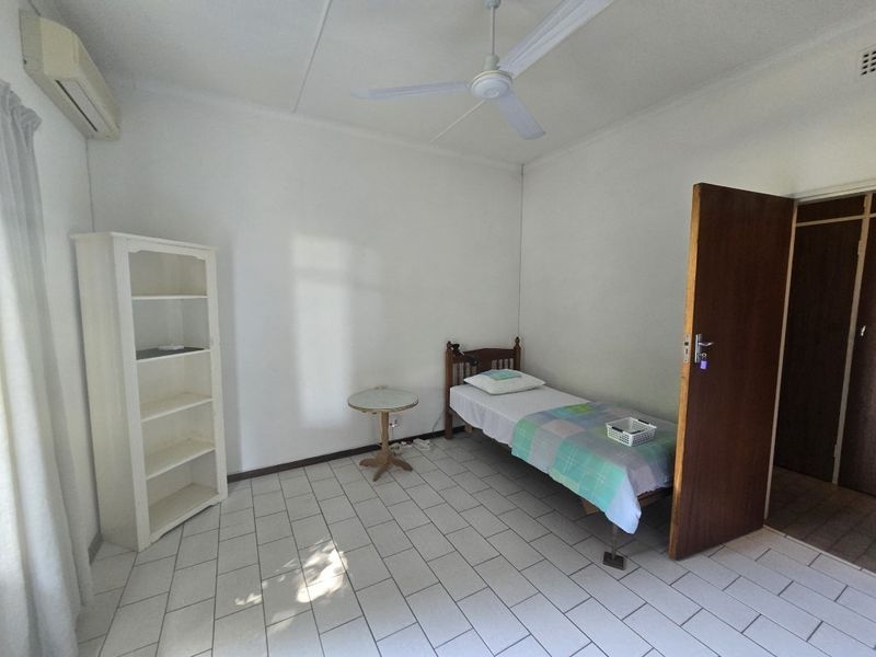 A simple bedroom featuring tiled flooring, a ceiling fan, and a wall-mounted air conditioning unit.