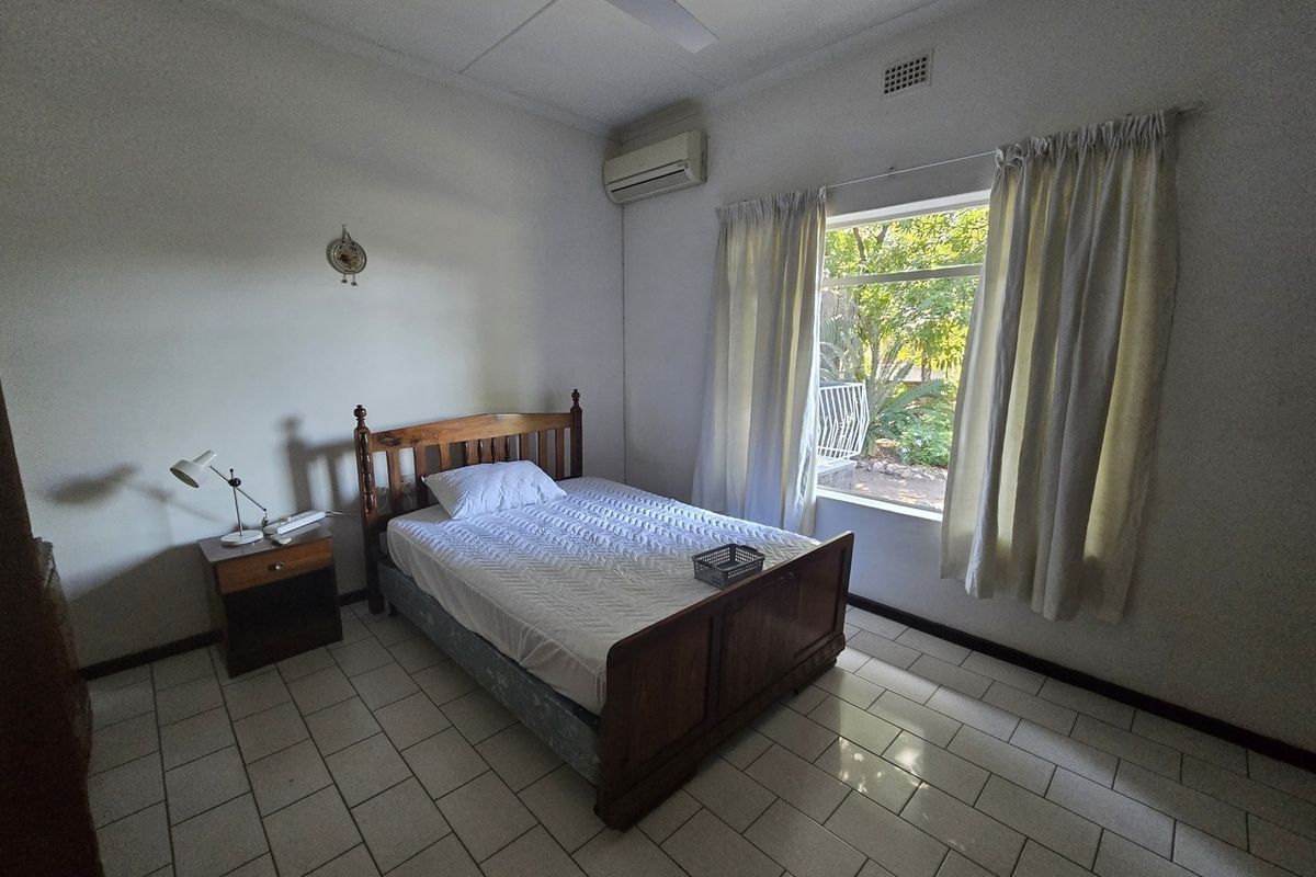 A functional bedroom featuring tiled flooring, a ceiling fan, and a wall-mounted split-system air conditioner with natural light from a large window.