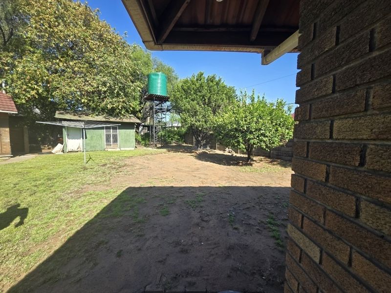 A spacious rear garden featuring a brick exterior wall, a raised water tank, an outbuilding, and a rotary clothesline.