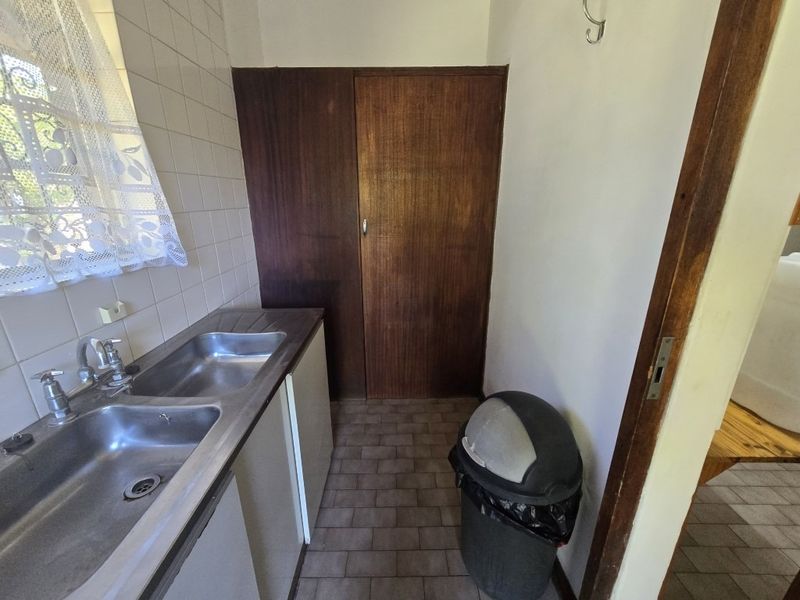 A functional scullery area featuring a double stainless steel sink, tiled splashback, and built-in cabinetry with a tiled floor.