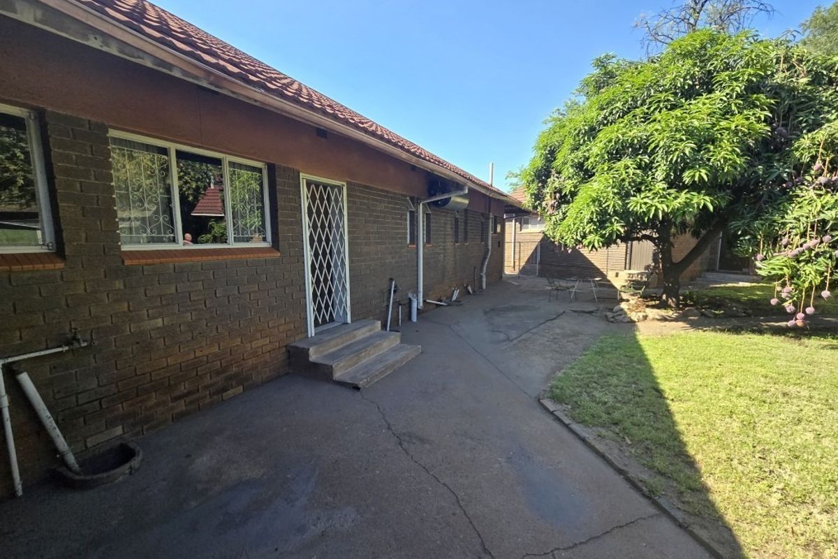 Rear view of the house featuring a brick facade, tiled roof, security gate, and concrete paved area leading to the garden.