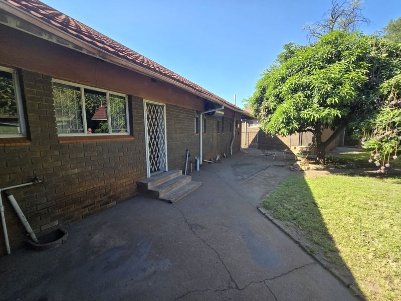 Rear view of the house featuring a brick facade, tiled roof, security gate, and concrete paved area leading to the garden.