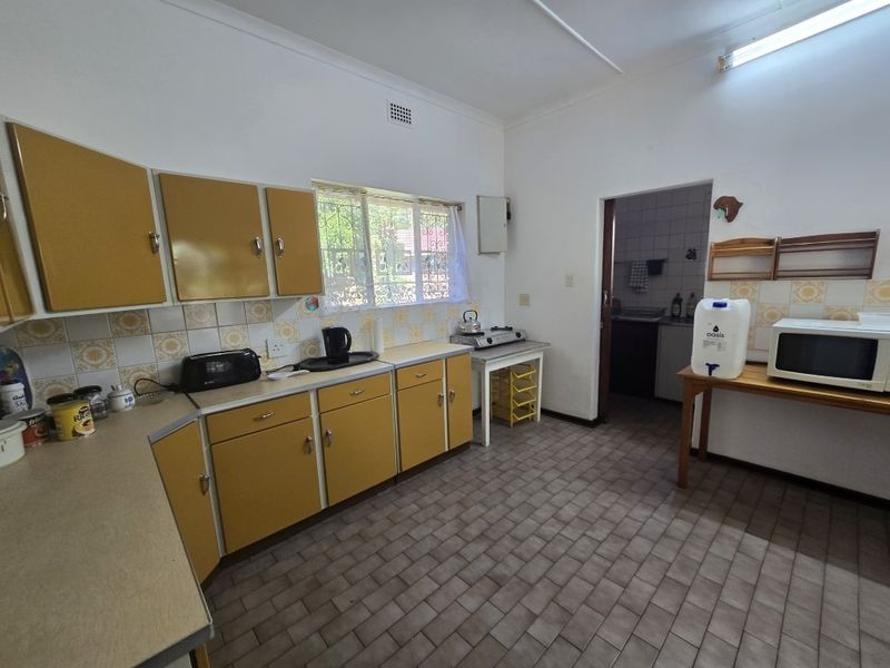 A functional kitchen featuring original cabinetry, tiled backsplash, and tiled flooring, with an adjacent scullery area visible through the doorway.