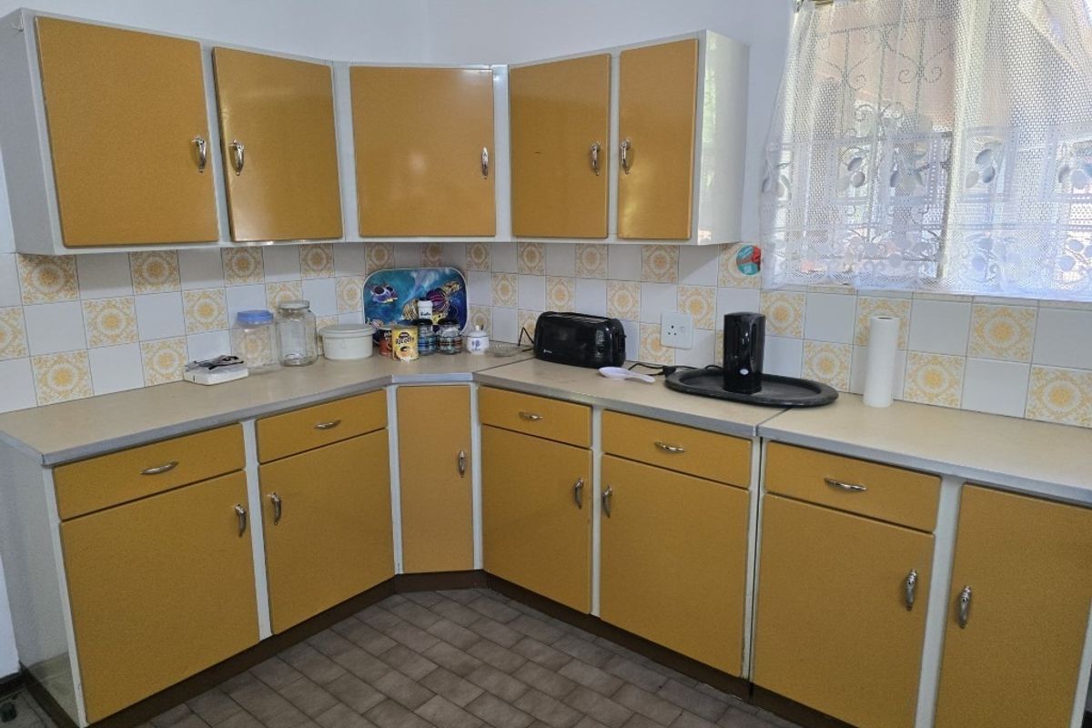 A functional kitchen featuring dated yellow cabinetry, laminate countertops, and a tiled backsplash, offering significant potential for a modern renovation.