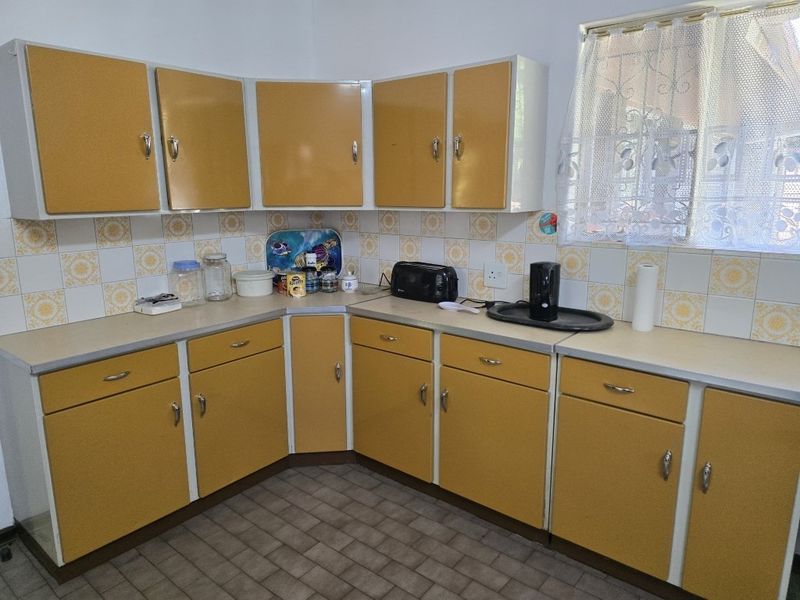 A functional kitchen featuring dated yellow cabinetry, laminate countertops, and a tiled backsplash, offering significant potential for a modern renovation.