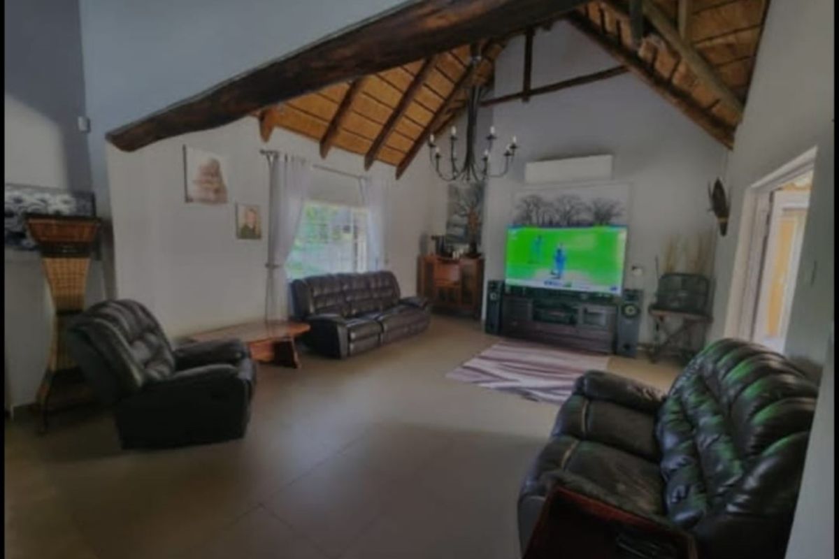 Spacious living room featuring a high vaulted ceiling with exposed timber beams, tiled flooring, and a wall-mounted air conditioning unit.