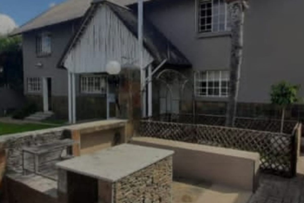 Rear exterior view featuring a built-in stone braai area, paved patio, and access to the multi-story dwelling with a thatched roof.