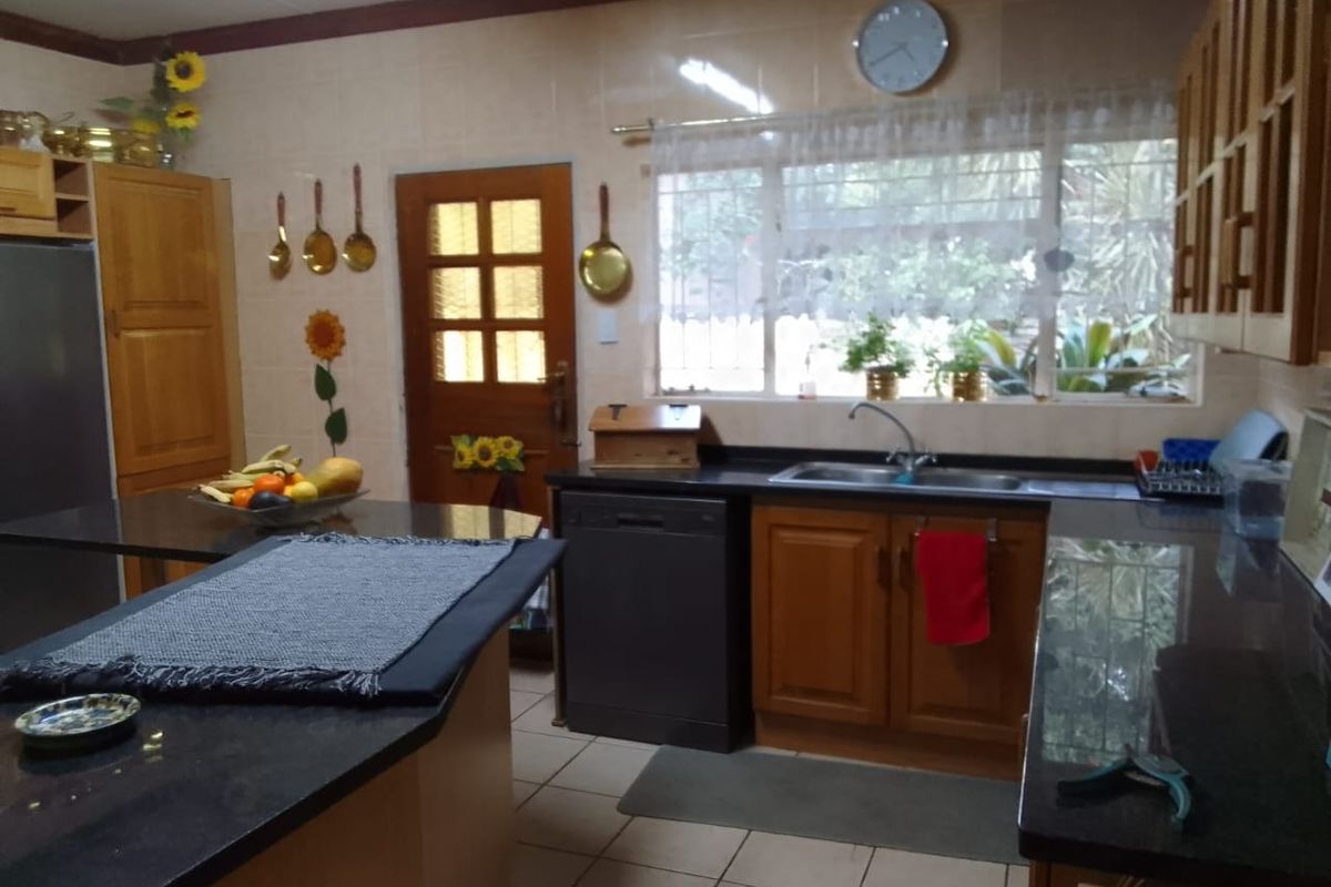 A functional kitchen featuring wooden cabinetry, dark granite countertops, a double sink, and tiled flooring with direct access to the exterior.