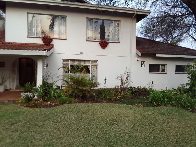 A two-story residential house featuring a white facade, tiled roof, and a well-maintained front garden with established landscaping.