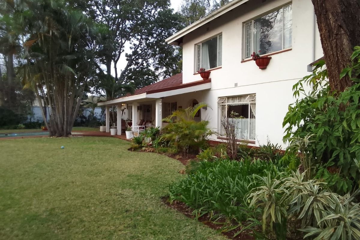 A view of the rear elevation of the house, featuring a covered patio, landscaped garden, and mature trees.