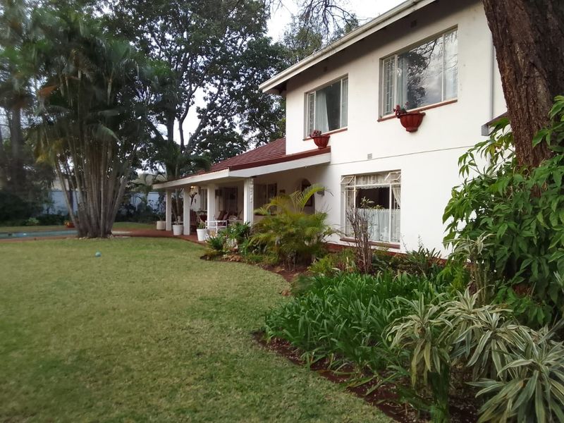 A view of the rear elevation of the house, featuring a covered patio, landscaped garden, and mature trees.