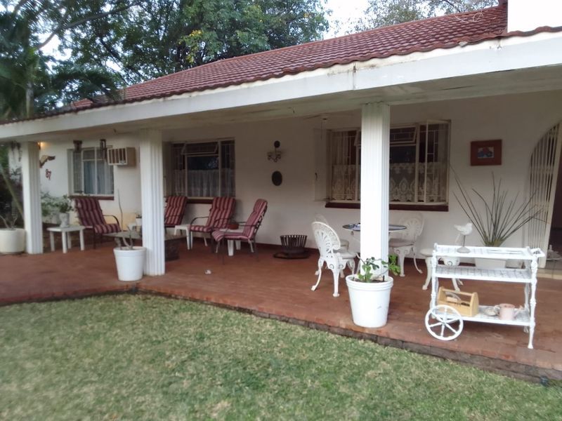 A covered patio area featuring classic columns, terracotta-style flooring, and direct access to the garden, providing a functional outdoor living space.