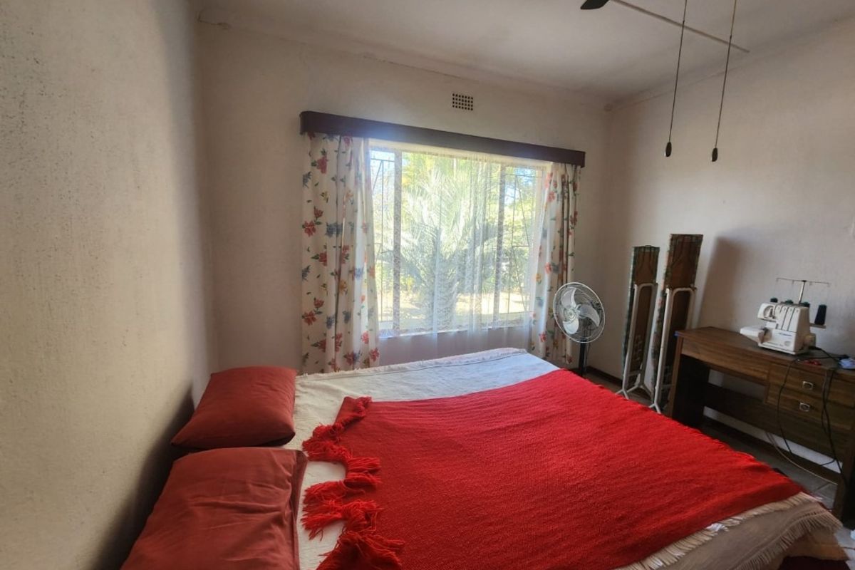 A bedroom featuring a large window with security bars, ceiling fan, and basic wall finishes.
