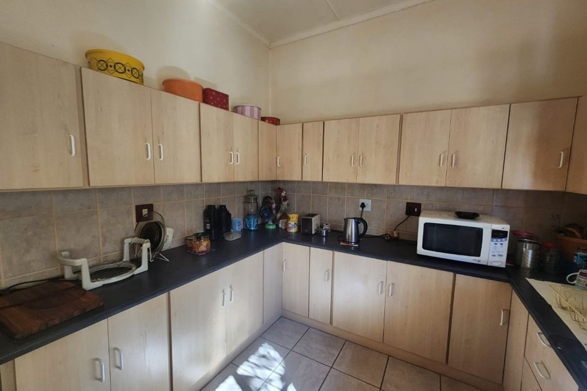 A functional kitchen featuring light wood-finish cabinetry, dark laminate countertops, and tiled flooring, providing ample storage and workspace.