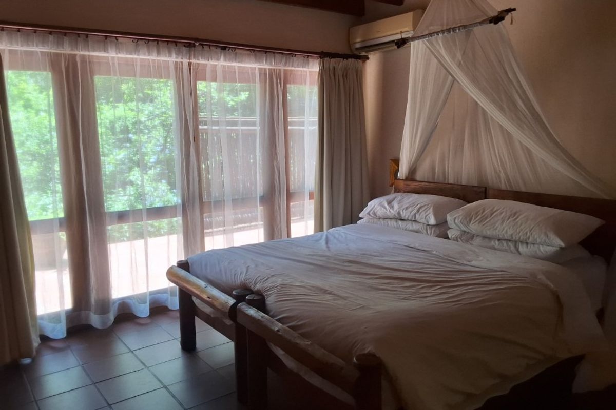 A bedroom featuring exposed timber ceiling beams, tiled flooring, and large glass sliding doors providing natural light and access to the exterior.