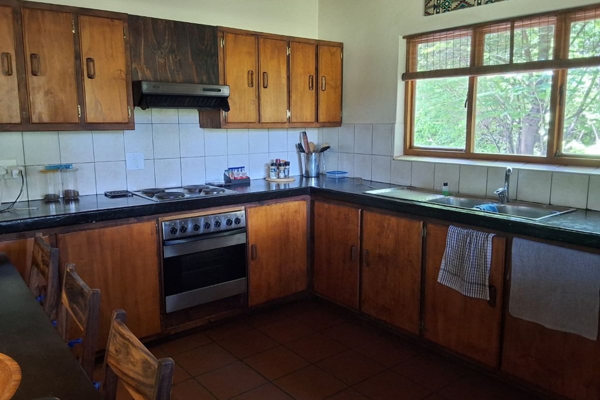 A functional kitchen featuring wooden cabinetry, a built-in oven with extractor fan, tiled backsplash, and a double basin sink with garden views.