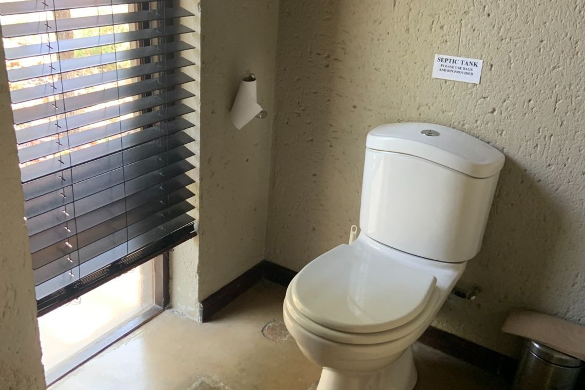 A functional bathroom featuring a standard toilet, textured wall finishes, and venetian blinds. The space requires cosmetic updates to improve its overall condition.