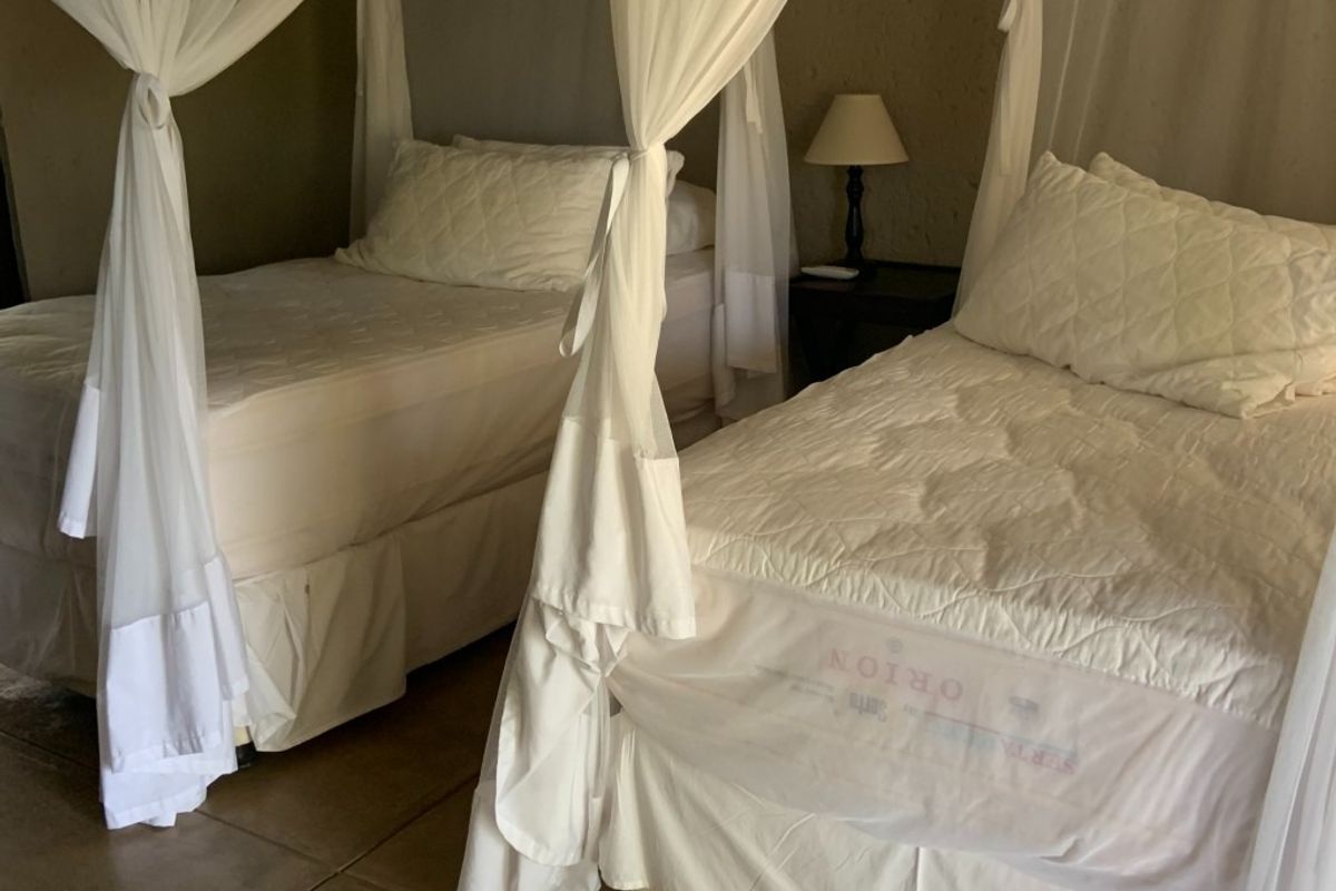 A bedroom featuring tiled flooring and two twin beds with canopy drapes.