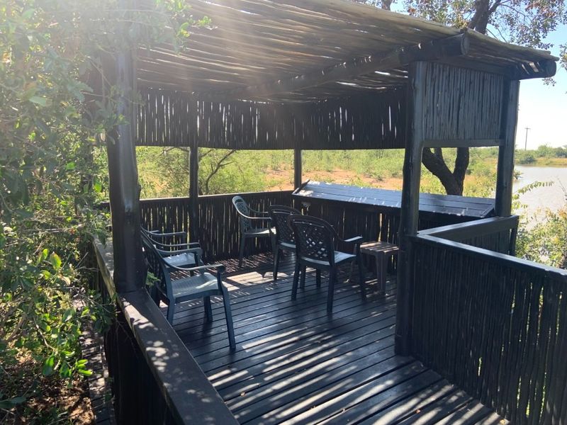 An elevated outdoor timber deck featuring a thatched roof, privacy screening, and a built-in bar counter overlooking the surrounding natural landscape.