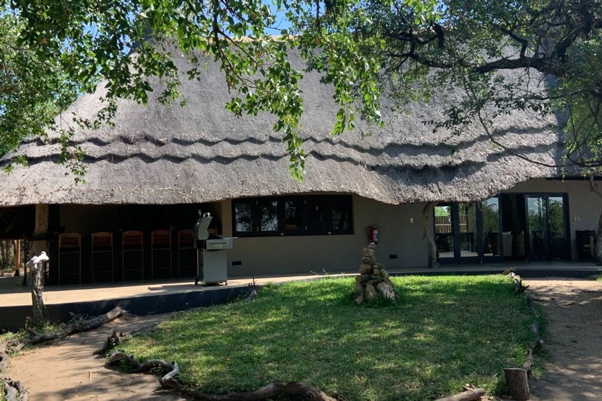 Rear exterior view of a property featuring a traditional thatched roof, a covered patio area with a built-in bar, and a landscaped garden.