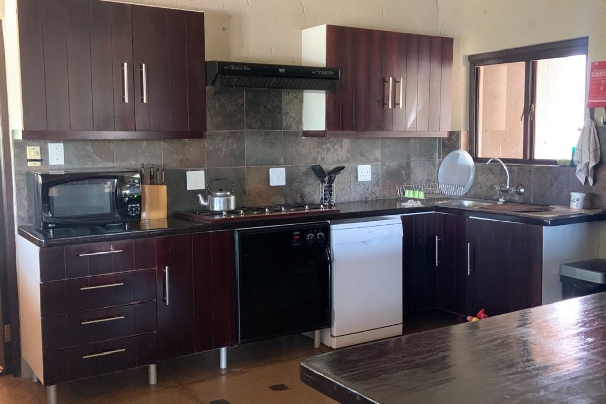 A functional kitchen featuring dark wood cabinetry, stone tile backsplash, built-in gas hob, extractor fan, and a stainless steel sink with laminate countertops.