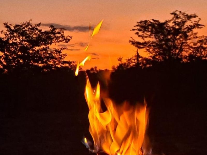 A scenic view of a sunset over the farm landscape with a campfire in the foreground.