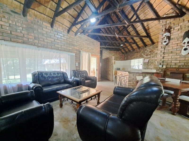 Open plan living and kitchen area featuring exposed brick walls, a high thatched ceiling with timber trusses, and a built-in brick breakfast bar.