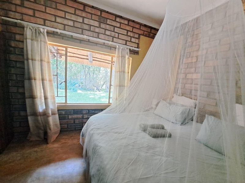 A rustic bedroom featuring exposed brick walls, concrete flooring, and a large window overlooking the garden.