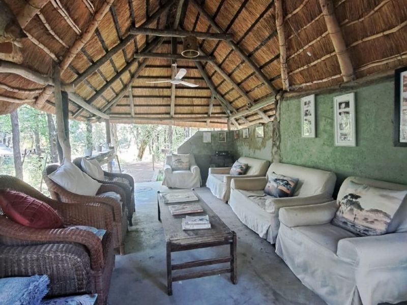 Rustic outdoor patio area featuring a traditional thatched roof with exposed timber rafters, concrete flooring, and a ceiling fan, ideal for relaxed outdoor living.