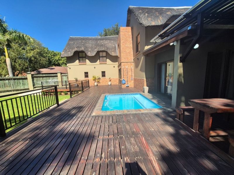 Spacious outdoor entertainment area featuring a swimming pool set within extensive timber decking, adjacent to a multi-story house with a traditional thatch roof.