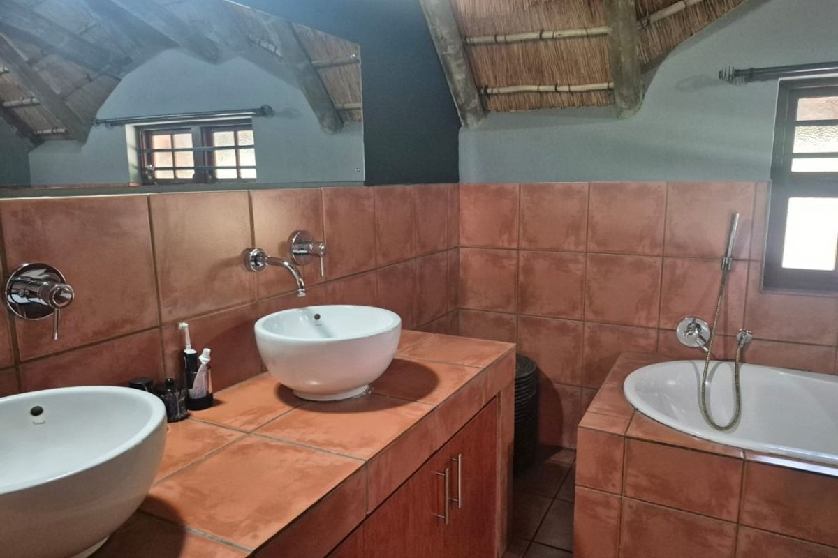 Bathroom featuring a double vanity with vessel sinks, wall-mounted faucets, and a built-in bathtub, set under a unique thatched roof ceiling.