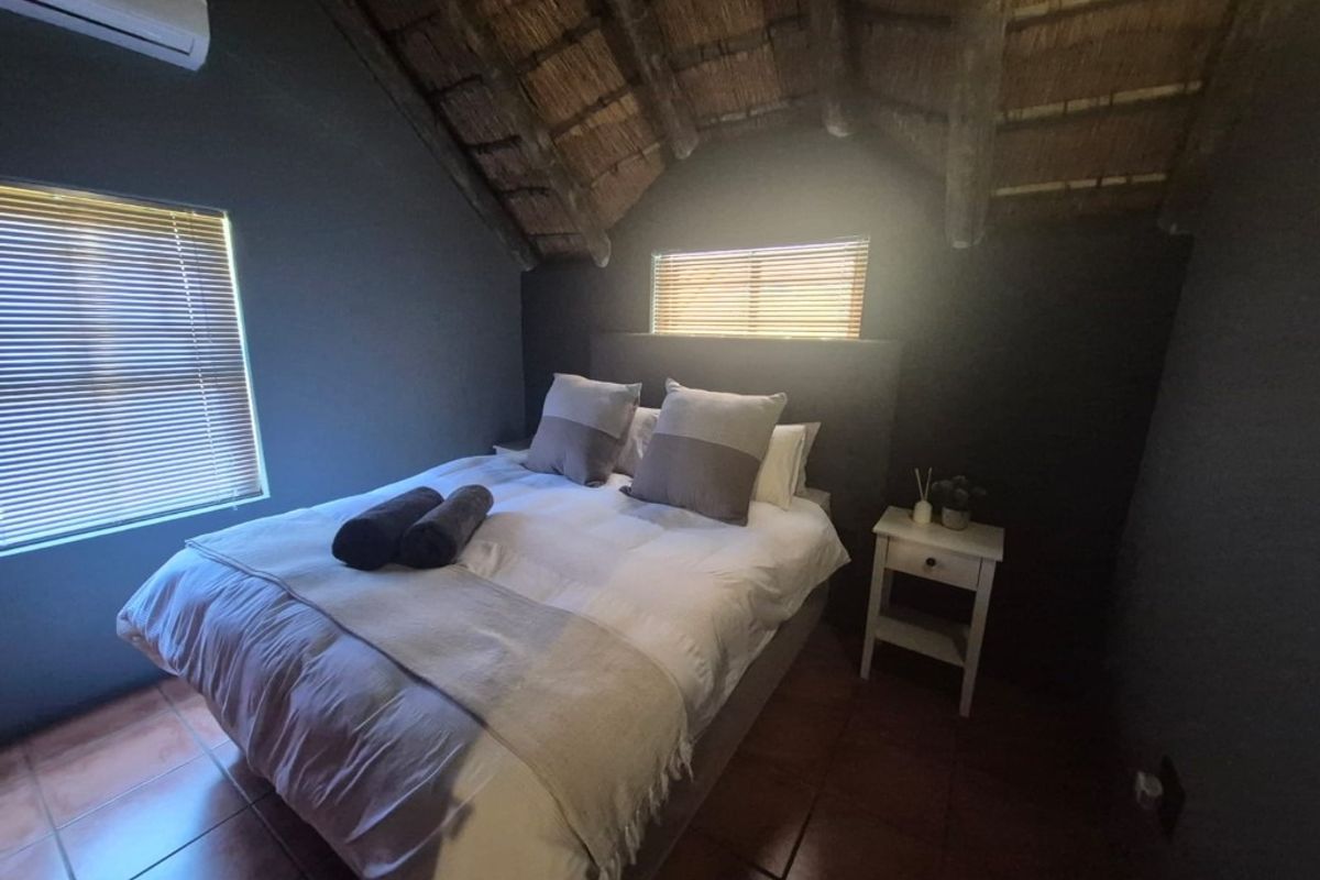 A cozy bedroom featuring a rustic exposed thatch ceiling with timber rafters, tiled flooring, and a wall-mounted air conditioning unit.
