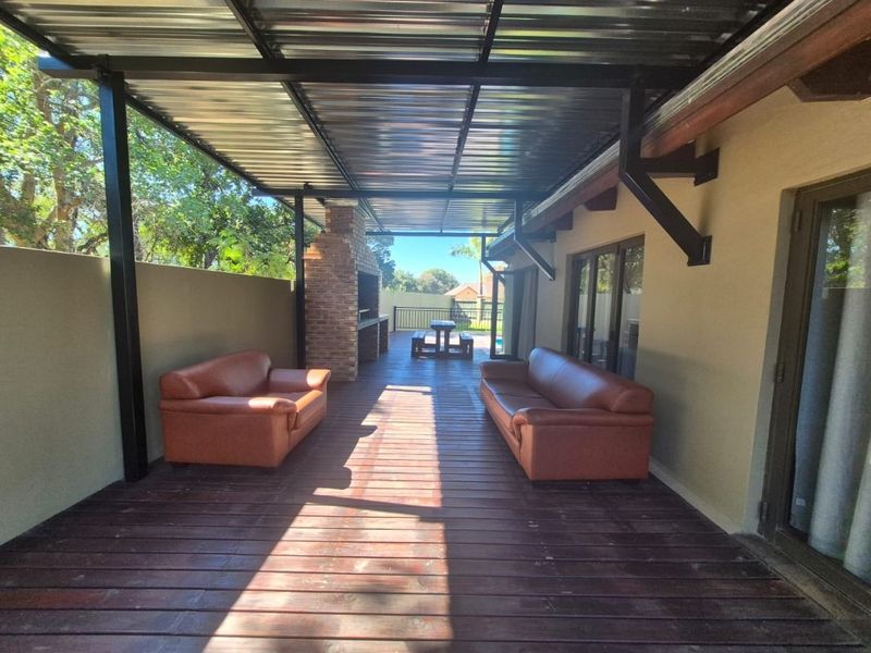 Spacious covered patio featuring timber decking and a built-in brick braai, providing an ideal outdoor entertainment area overlooking the garden.
