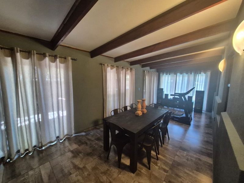 Dining room featuring exposed timber ceiling beams, tiled flooring, and multiple sliding glass doors providing natural light and access to the exterior.