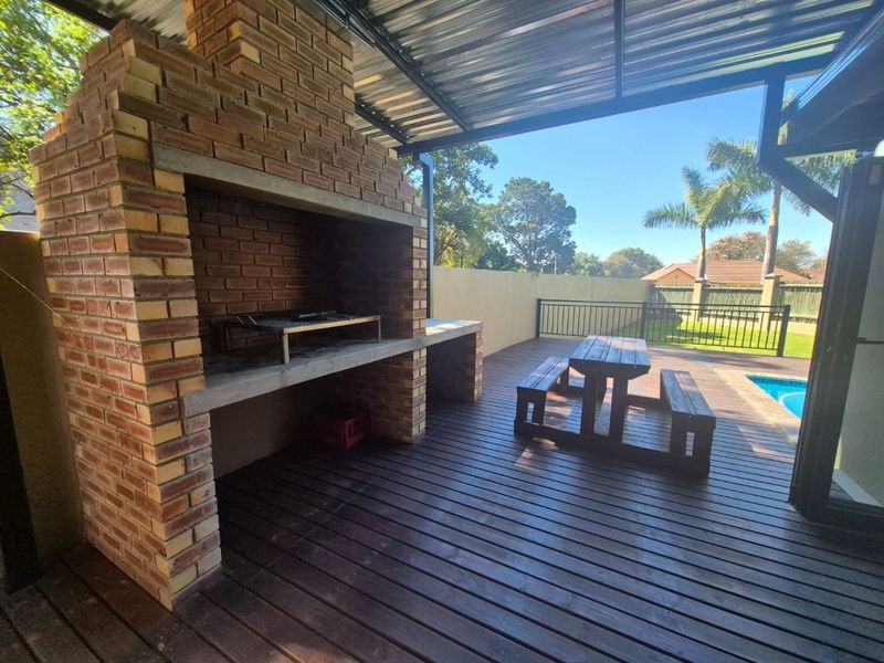 Covered outdoor patio featuring a built-in brick braai, timber decking, and direct access to the swimming pool area.