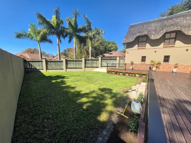 A spacious rear garden featuring a well-maintained lawn, timber decking with metal balustrades, and a distinctive thatched roof building facade.