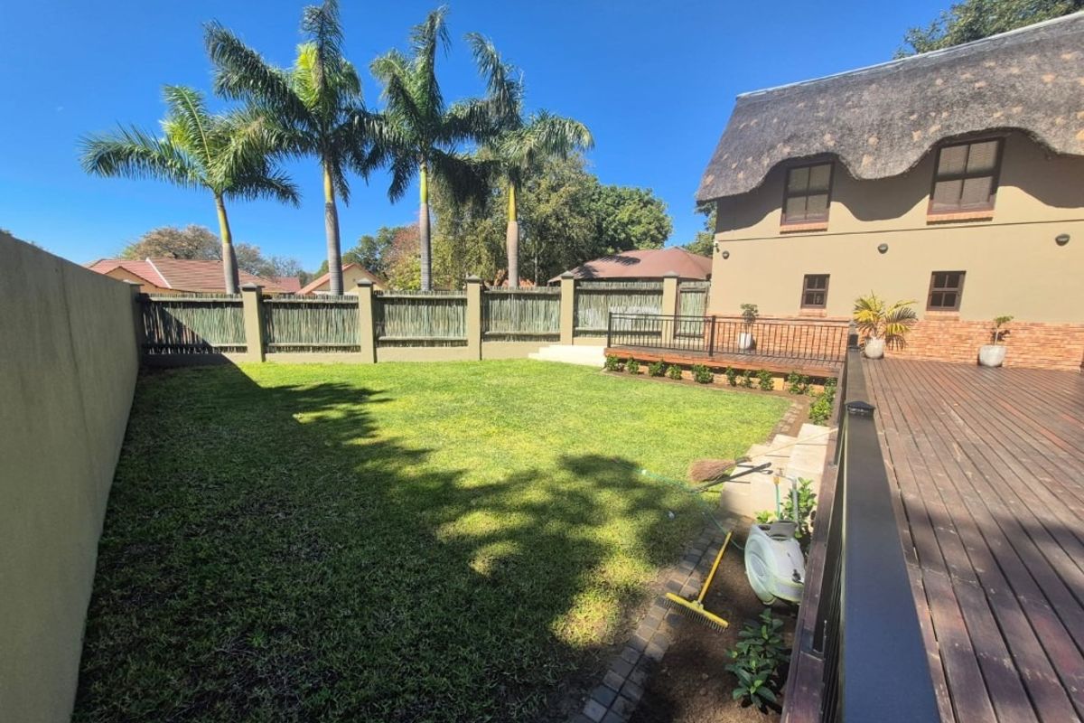 A spacious rear garden featuring a well-maintained lawn, timber decking with metal balustrades, and a distinctive thatched roof building facade.