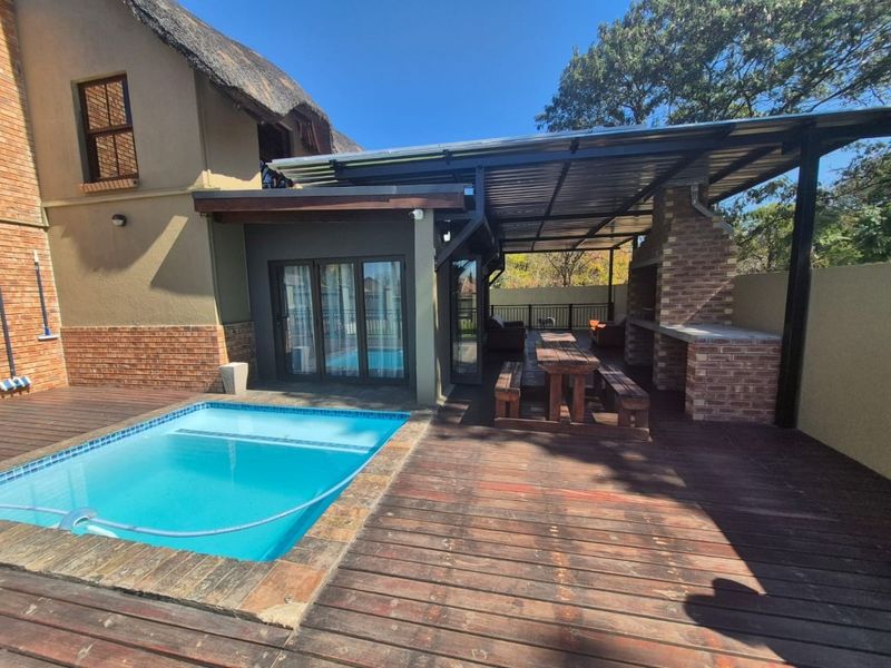 Outdoor entertainment area featuring a covered patio with a built-in brick braai, timber decking, and an adjacent swimming pool.