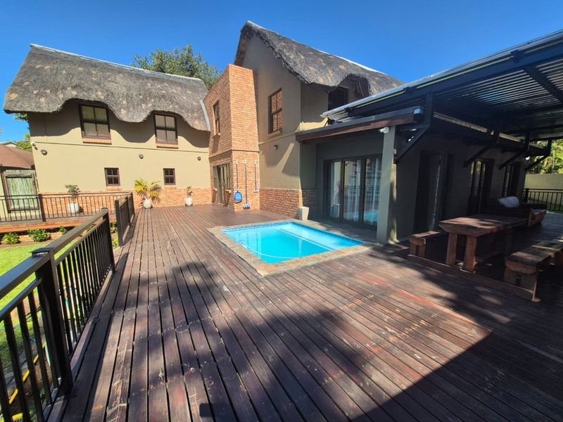 Spacious outdoor entertainment area featuring a swimming pool, extensive timber decking, and a covered patio attached to a characterful thatched-roof home.