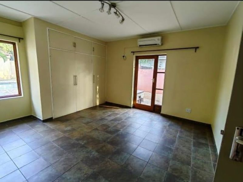 Spacious bedroom featuring tiled flooring, built-in cupboards, a split-system air conditioner, and direct access to the exterior through a glass panel door.