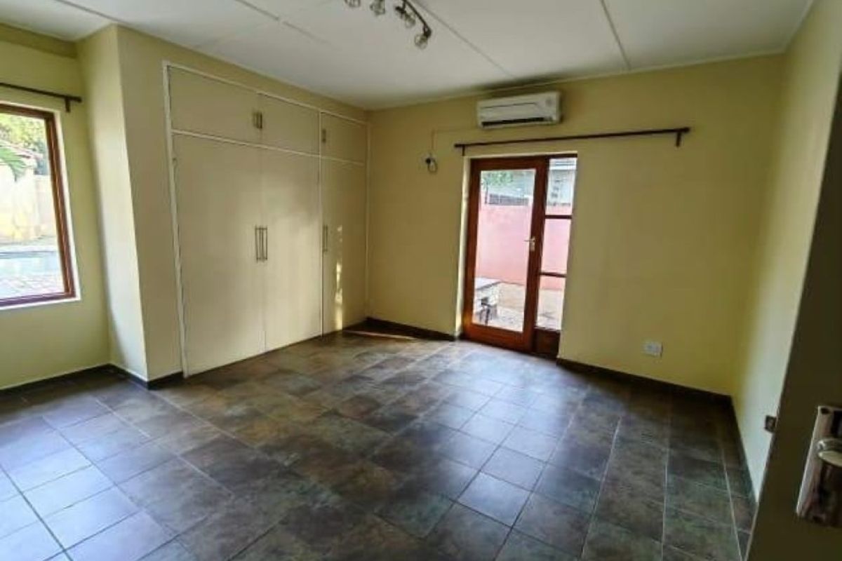 Spacious bedroom featuring tiled flooring, built-in cupboards, a split-system air conditioner, and direct access to the exterior through a glass panel door.