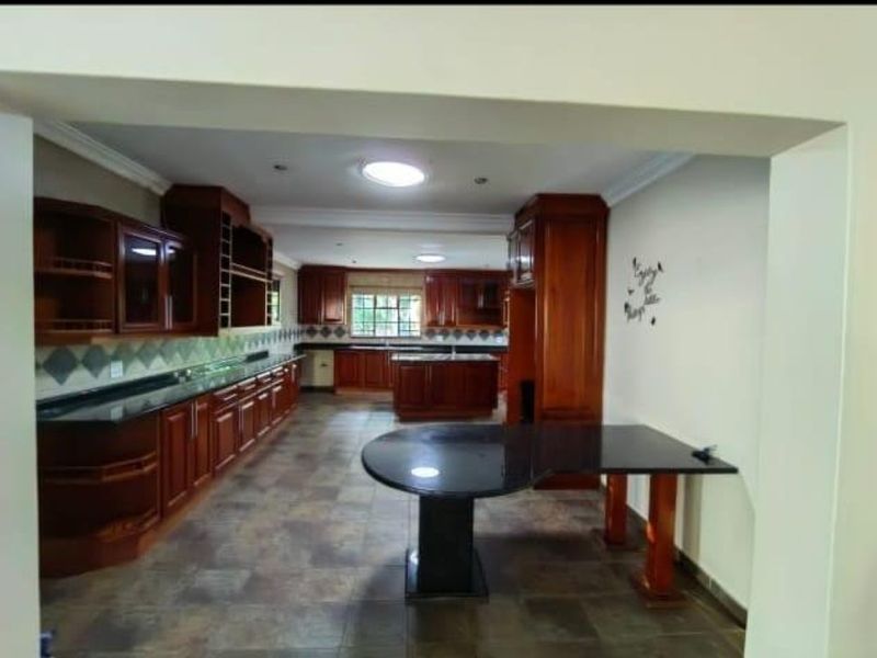 Spacious kitchen featuring extensive wooden cabinetry, granite countertops, a central island, and tiled flooring, illuminated by natural light from skylights.