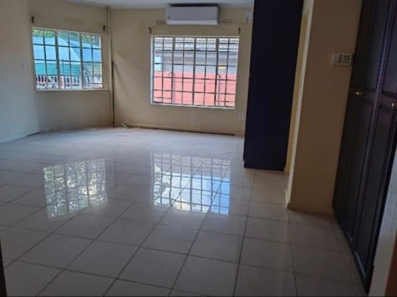 Spacious, empty living area featuring polished tiled flooring, a wall-mounted air conditioning unit, and built-in storage cupboards.
